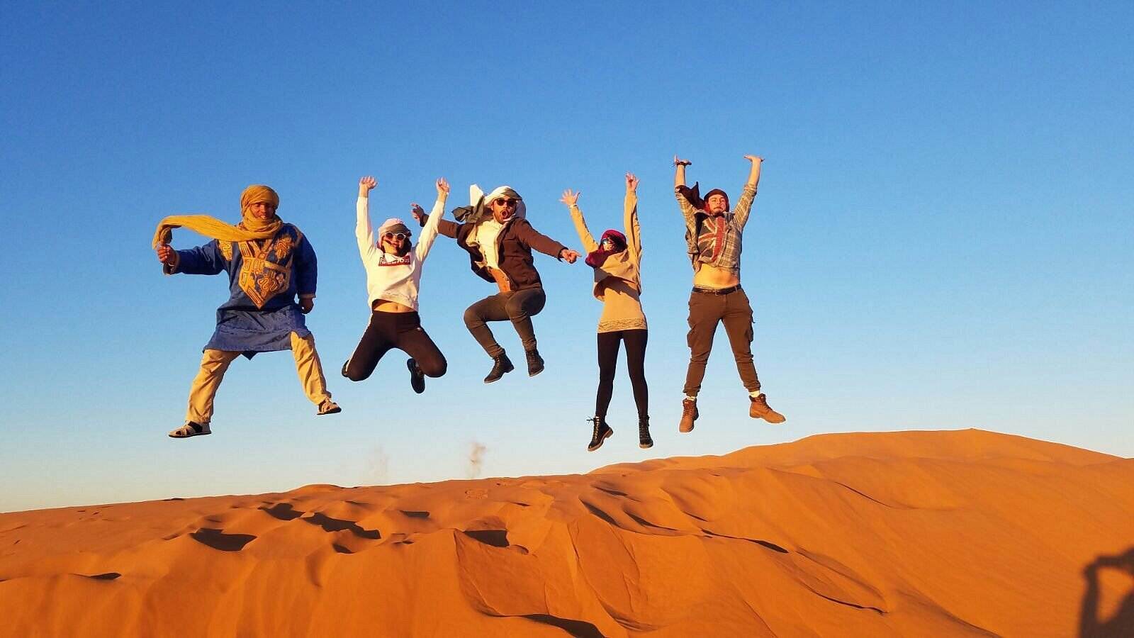 Travelers jumping on a Sahara dune with their Touareg guide
